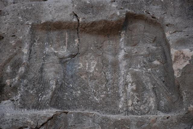 شاه ساسانی ساقه یک گل را با دو انگشت گرفته و به زنی می‌دهد. او یا همسرش است یا خدایبانوی آب (آناهیتا)